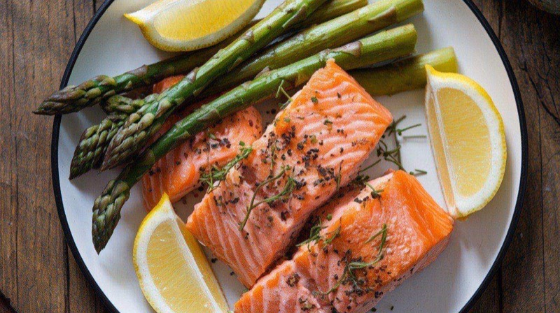 Golden crispy air fryer salmon bites arranged on a plate with lemon wedges, steamed asparagus, and brown rice