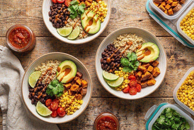 Colorful burrito bowl with quinoa, black beans, yellow corn, diced red pepper, and fresh cilantro in a round meal prep container