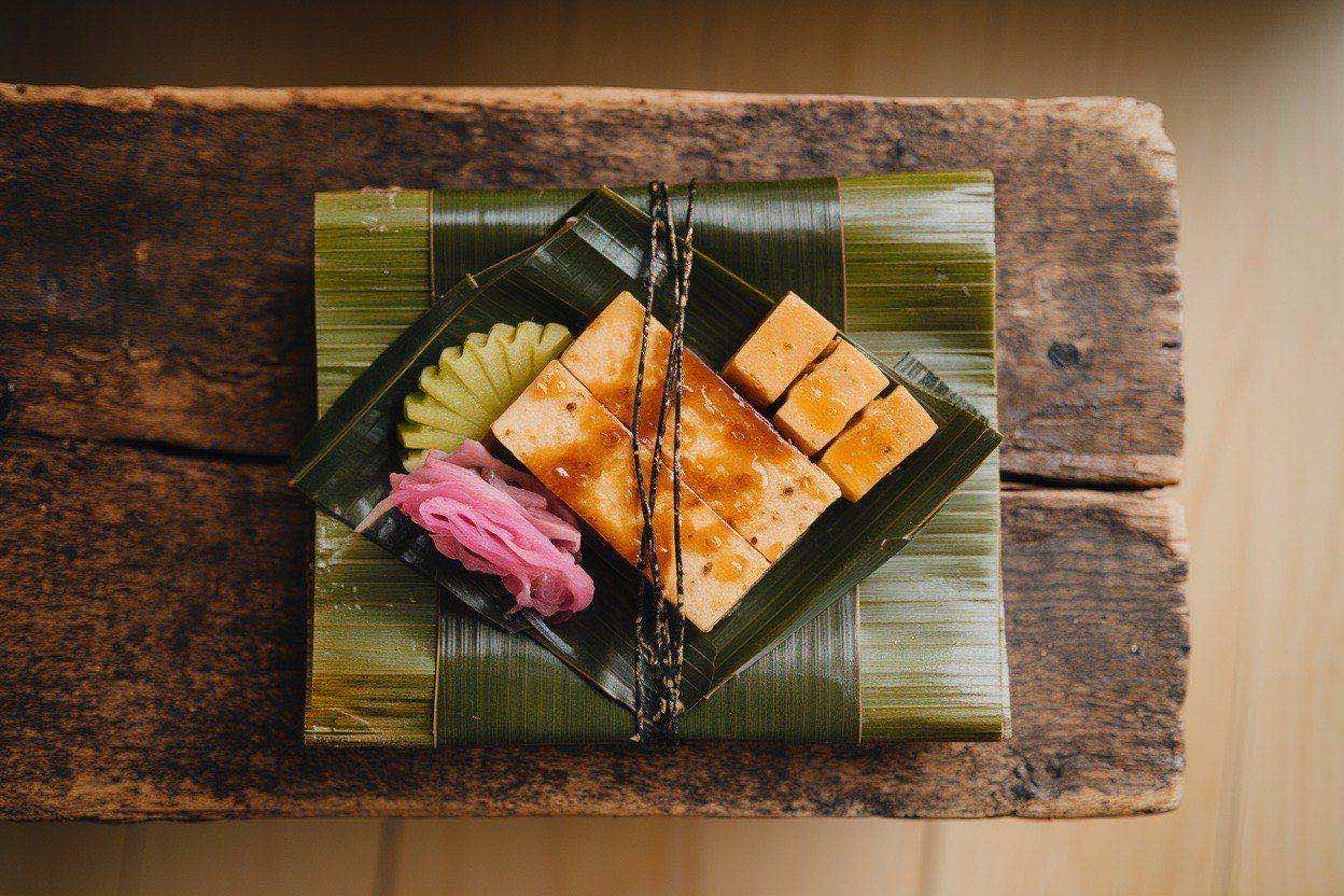 Neatly arranged bento box with glazed teriyaki tofu slices, sesame-sprinkled rice, bright green edamame, and pink pickled ginger