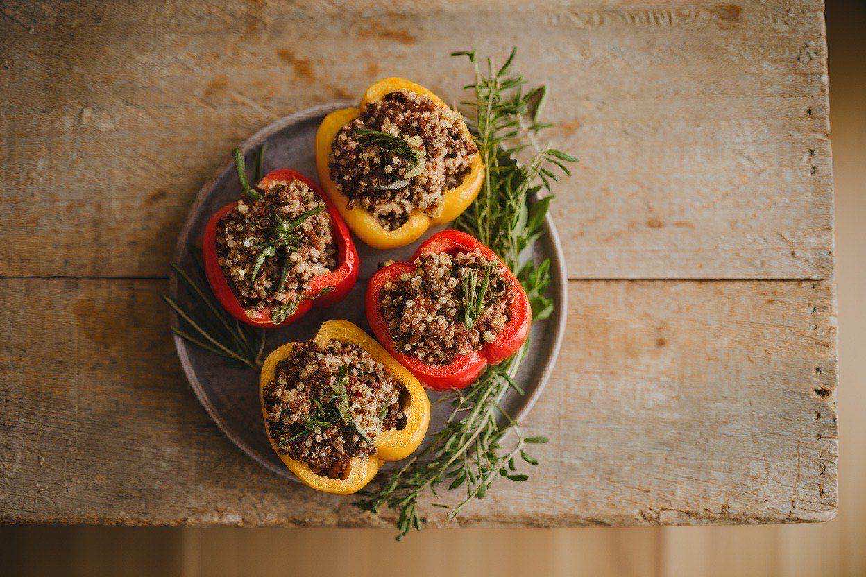 Six colorful quinoa-stuffed bell peppers in a baking dish, showing the quinoa, black bean, and corn filling