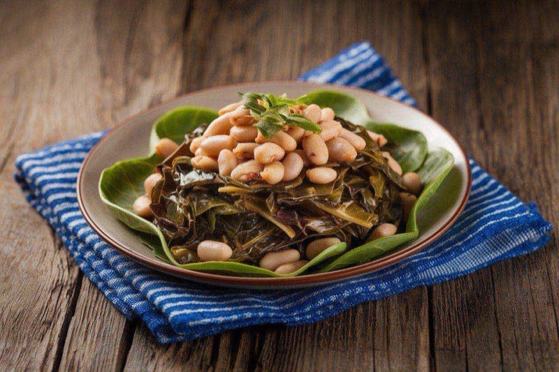 Bowl of tender dark green collard greens with white beans in a rich smoky broth