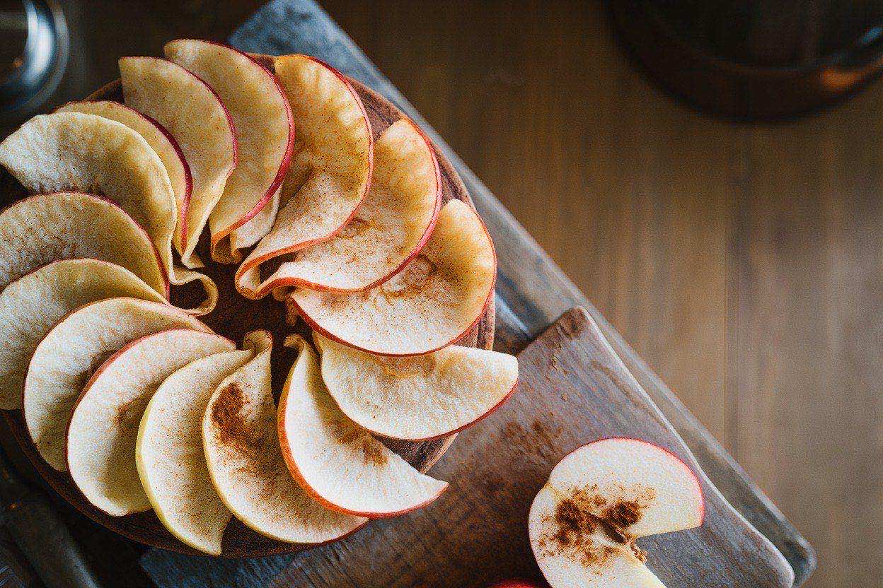 Thin, translucent apple chips with cinnamon dusting arranged in a bowl