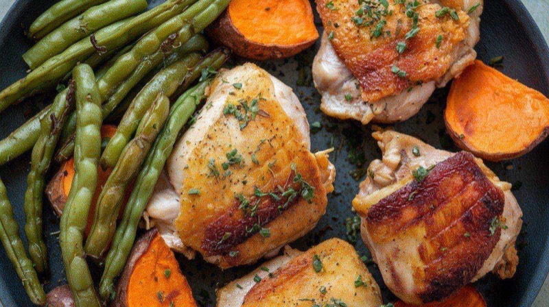 Golden brown air-fried chicken thighs with perfectly crispy skin arranged on a white plate with fresh herbs