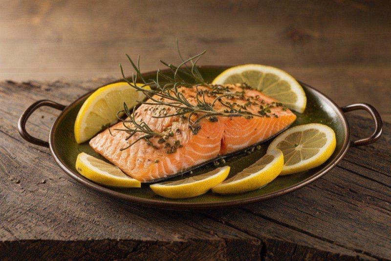 Golden roasted salmon fillets topped with lemon slices surrounded by roasted asparagus and cherry tomatoes